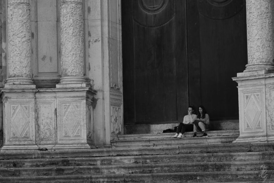 wo girls sitting in front of a huge door to the cathedral in Cadiz